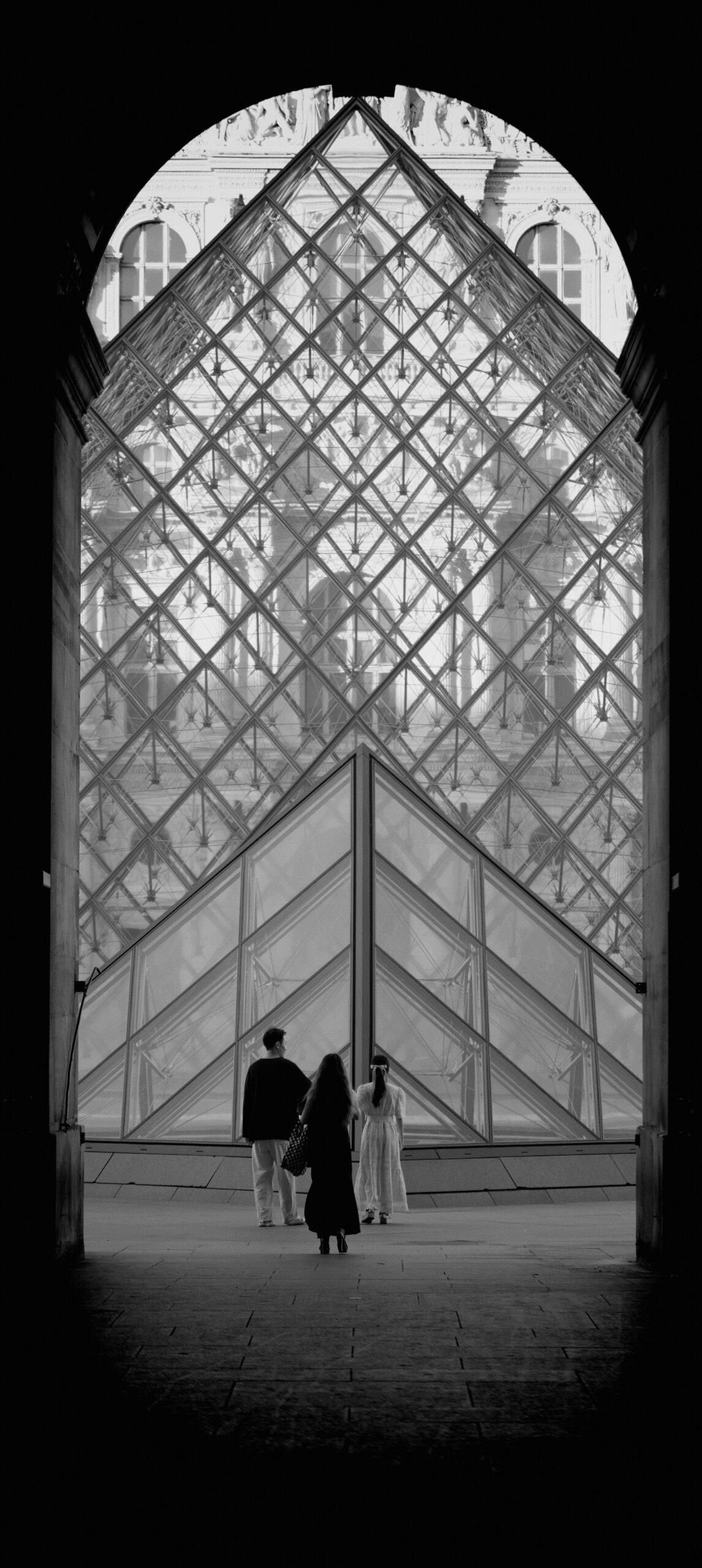 Vue de la pyramide du Louvre depuis un couloir. Un couple pose devant.